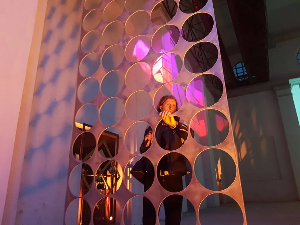 Francesco Lussana dietro una sua opera scultorea in metallo alla ex centrale termoelettrica di Daste e Spalenga — cerchi forati illuminati di magenta e blu, Civiltà Industriale SUONO E LUCE