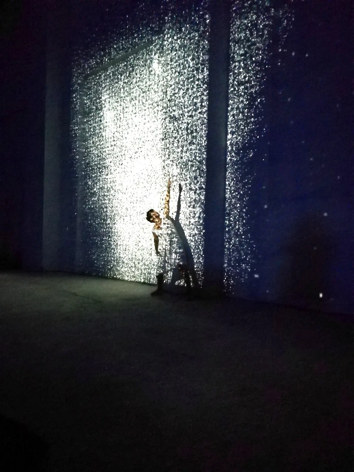 Danzatrice con braccio alzato immersa in scie di comete, onde e galassie proiettate sulla parete industriale — danza contemporanea e proiezioni interattive, Danza Liquida SUONO E LUCE