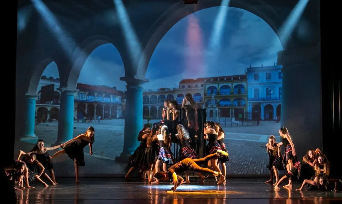 Grande ensemble di danzatori con videoproiezione di piazza porticata e fasci di luce — produzione tecnica per spettacolo di danza, SUONO E LUCE