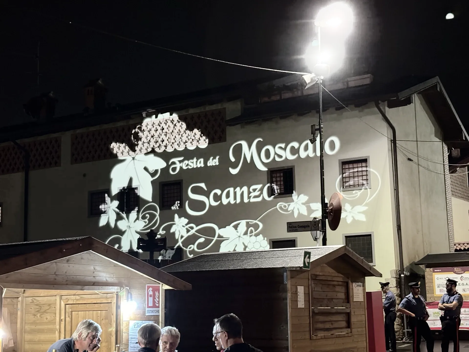 Maxiproiezione 'Festa del Moscato di Scanzo' su facciata con casette del mercato — SUONO E LUCE