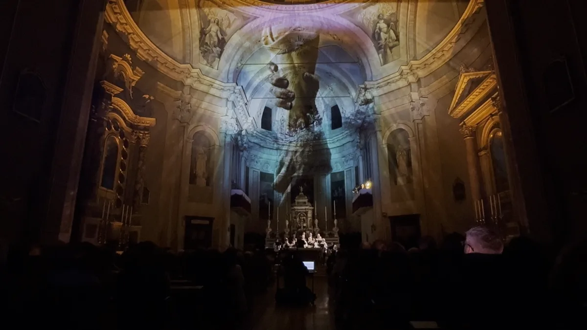 Scultura classica gigante proiettata sull'abside di una chiesa — luci calde rivelano l'architettura, spettacolo immersivo Luccicanti SUONO E LUCE